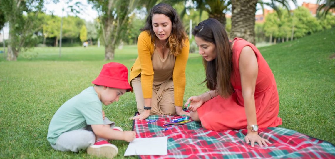 A child and two women enjoying a drawing session on a picnic blanket in a park in Portugal.